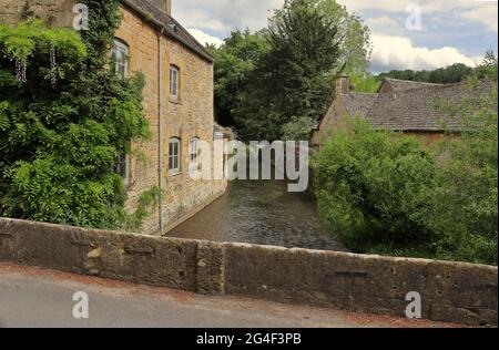 Il fiume Windrush che scorre sotto un ponte stradale nel villaggio Cotswold di Naunton in Gloucestershire, Regno Unito Foto Stock