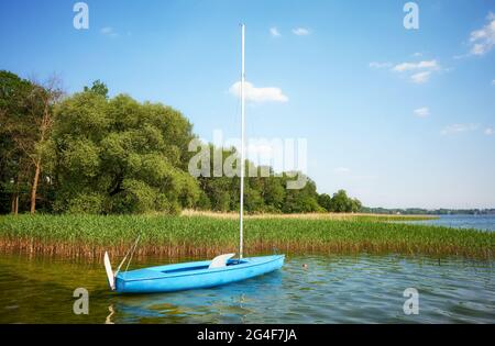 Piccola barca a vela blu ormeggiata da canne, Lago di Drawsko, Polonia. Foto Stock