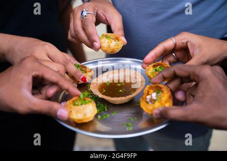 Primo piano, gruppo di amici mani che prendono Pani puri spuntini dal piatto - concetto di condivisione del cibo o indiano sera cibo di strada. Foto Stock
