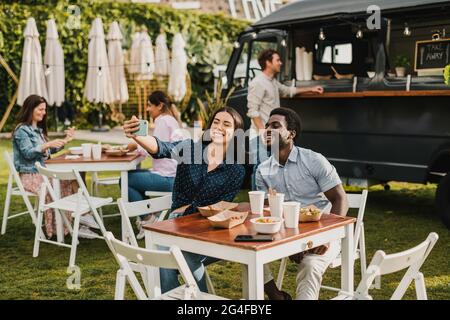 Amici diversi che prendono selfie fuori camion cibo Foto Stock