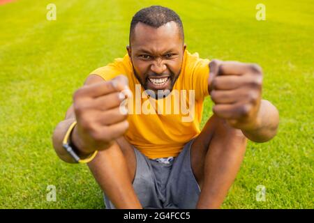 Primo piano di gioioso afro uomo che inizia a correre su pista moderna. Ritratto di jogging emozionale su pista in slow motion. Ragazzo giovane che si esercita a. Foto Stock
