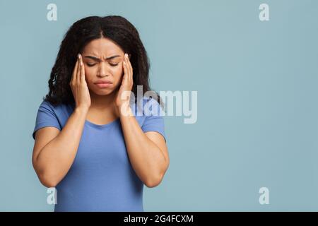 Concetto di emicrania e mal di testa. Donna afroamericana che soffre di ipertensione su sfondo blu studio Foto Stock