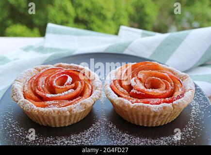 Coppia di gustosi e sani mini tartlets di Rosa di mela con il foliage verde sfocato in background Foto Stock