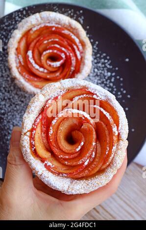 La mano della donna che raccoglie una splendida mini torta di rose di mela cosparsa di zucchero a velo Foto Stock