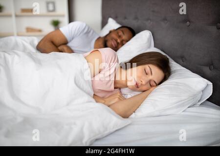 Giovane donna caucasica e il suo marito nero che dormono insieme a letto a casa. Rapporto amorevole Foto Stock