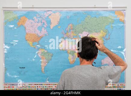 Giovane uomo adulto guardando la mappa del mondo con la mano sulla sua testa Foto Stock