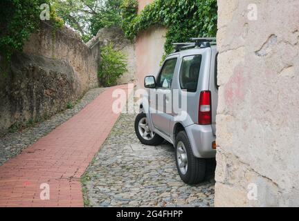 Un SUV parcheggiato su un vicolo acciottolato murato in Italia Foto Stock