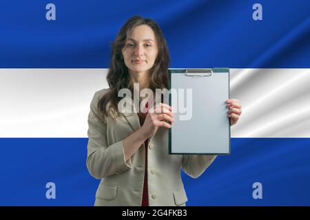 Studiare a El Salvador. Bella donna che tiene un foglio di carta nelle sue mani. Ragazza sullo sfondo della bandiera di El Salvador. Foto Stock