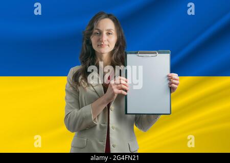 Studio in Ucraina. Bella donna che tiene un foglio di carta nelle sue mani. Ragazza sullo sfondo della bandiera dell'Ucraina. Foto Stock