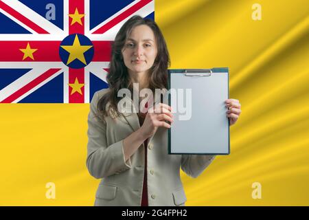 Studiare a Niue. Bella donna che tiene un foglio di carta nelle sue mani. Ragazza sullo sfondo della bandiera di Niue. Foto Stock