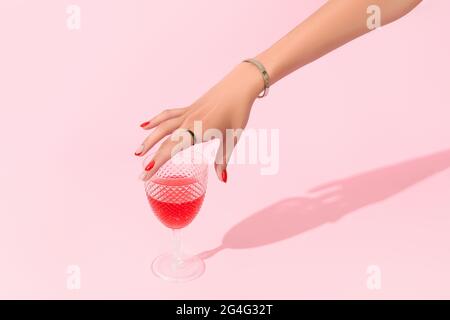 Womans mano che tiene il vetro su sfondo rosa. Tendenze di progettazione di manicure Foto Stock