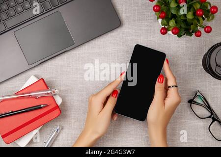 Donna con manicure rosso che tiene il telefono cellulare sul tavolo grigio Foto Stock