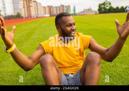 Giovane bel sportivo afroamericano uomo in giallo sport indossare calmo spensierato ed eccitato allo stadio campo erba, celebrando la vittoria. Vittoria Foto Stock