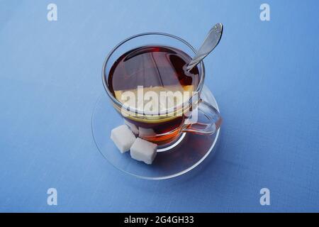 un bicchiere di tè con limone e due pezzi di zucchero si trova su un piatto di vetro su sfondo blu. Foto Stock