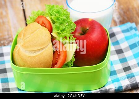 Una sana scatola per il pranzo della scuola contenente un rotolo di formaggio, lattuga e pomodoro, un bicchiere di latte di mela rossa Foto Stock