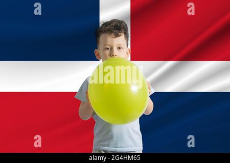 Giornata dei bambini nella Repubblica Dominicana Bianco ragazzo con un pallone sullo sfondo della bandiera della Repubblica Dominicana Festa dei bambini concetto. Foto Stock