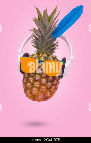 Carta d'invito estiva creativa con ananas che indossa occhiali da sole fatti di arancio fresco e cuffie su sfondo rosa. Scena minima di divertimento, festa, Foto Stock