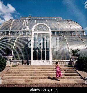 Giovane ragazza in abito rosa che corre verso la Plalm House al Royal Botanic Gardens, Kew, Londra, Inghilterra Foto Stock