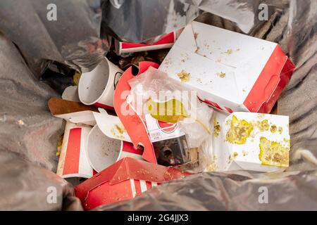 Bidone di rifiuti con i resti di confezione di cibo usa e getta e bicchieri di bevande analcoliche. Concetto di ecologia e conservazione dell'ambiente Foto Stock