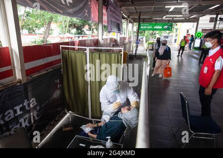 Un operatore sanitario vestito con tuta protettiva conduce un test antigenico su un passeggero alla stazione Manggarai di Giacarta. PT KAI Commuter Indonesia ha condotto test casuali sull'antigene sui passeggeri KRL per prevenire la diffusione di Covid-19. La prova è stata effettuata in diverse stazioni quali Bekasi, Bogor, Cikarang, Tangerang, Manggarai, E Tanah Abang prendendo di mira 150-200 test antigenici al giorno. Covid-19 in Indonesia continua a salire e rompere i record. Lunedì (21/6/2021) sono stati registrati altri 14,536 casi. Sulla base dei dati del Ministero della Salute, questo nuovo caso porta il totale positivo Foto Stock