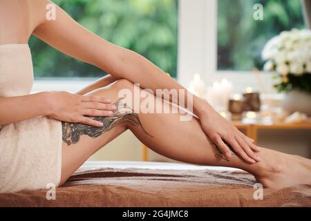 Primo piano di donna seduta in asciugamano e cura del suo corpo nel salone termale Foto Stock
