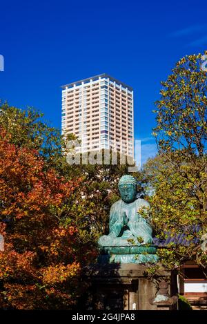 Giappone tra tradizione e modernità. Antico Grande Buddha di Yanaka con foglie autunnali e edificio moderno a Tokyo Foto Stock