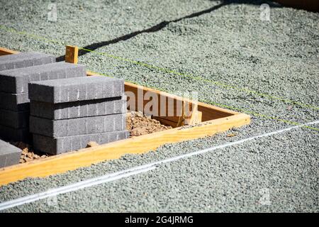 Le asfaltatrici in pietra grigia sono impostate accanto alla cassaforma in legno e alle stringhe di layout gialle. Messa a fuoco selettiva. Foto Stock