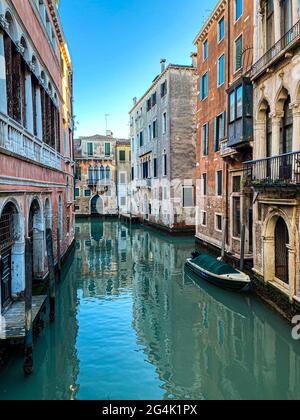Piccola barca su una strada canale a Venezia con belle case colorate, Italia. Cielo blu Foto Stock