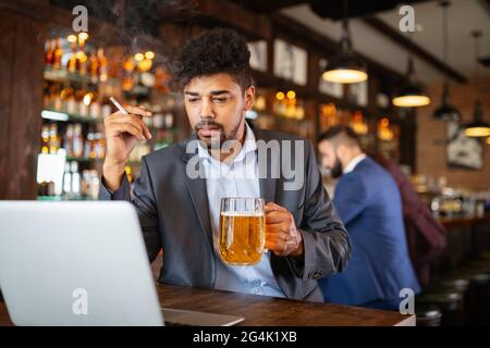 Uomo che beve birra e fuma sigaretta mentre lavora sul computer. Cattivo concetto di abitudine. Foto Stock