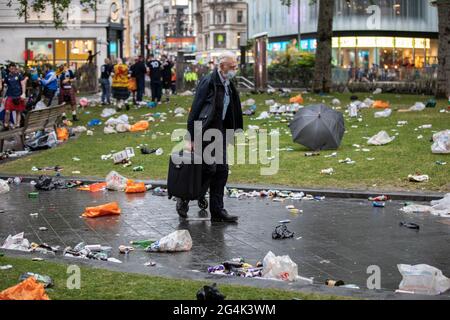 Un uomo che porta con sé la valigia da viaggio si fa strada attraverso tutte le bottiglie rotte e i rifiuti lasciati dietro dai tifosi di calcio scozzesi a Leicester Square Foto Stock