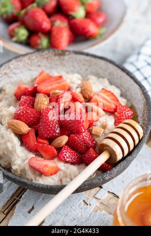 Porridge di farina d'avena con fragole, mandorle e miele su fondo di cemento. Vista in primo piano. Cibo sano per la colazione Foto Stock