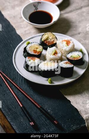 Panini fatti in casa con salmone, omelette giapponesi, avacado, wasabi e salsa di soia con bastoncini di legno su carta grigia su sfondo di legno nero Foto Stock