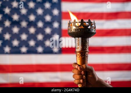 Primo piano di mani che tengono la torcia a fiamma olimpica con bandiera americana o americana come sfondo Foto Stock