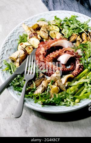 Insalata di pesce. Tentacoli grigliati di polpo, sardine e cozze su piatto di ceramica blu serviti con insalata di rucola, zucchine e asparagi Foto Stock