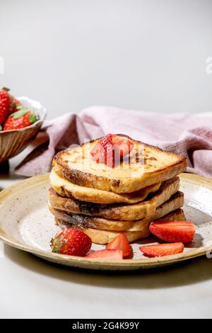 Cumulo di toast francesi con fragole fresche su piastra in ceramica e tovagliolo rosa su tavola bianca Foto Stock