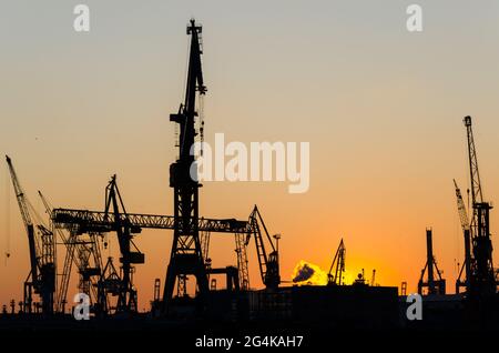 Sagoma di gru portuali e terminal container durante il tramonto panoramico ad Amburgo, Germania Foto Stock