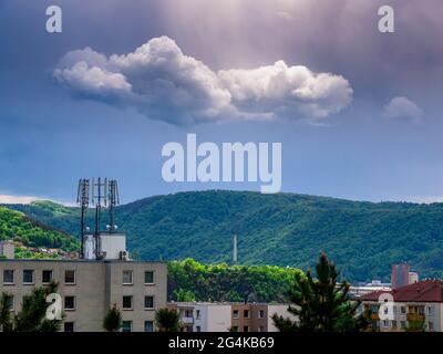 Trasmettitore di telecomunicazioni 5G sul tetto di un edificio di appartamenti con nuvole e luce del sole nel cielo scuro Foto Stock