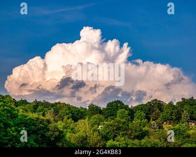 Enorme nube di pioggia - Cumulonimbus - che si forma nel cielo blu sopra collina boscosa Foto Stock