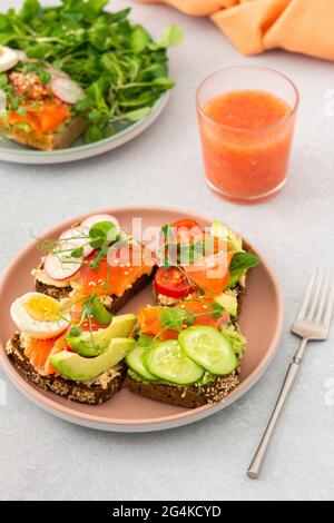 Sana e gustosa colazione, panini con avocado e salmone, cetrioli e pomodori, ravanelli e micrograni di piselli con uova sode e insalata di radice Foto Stock