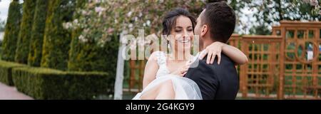 Sposo in tuta con allegra sposa nel parco, striscione Foto Stock