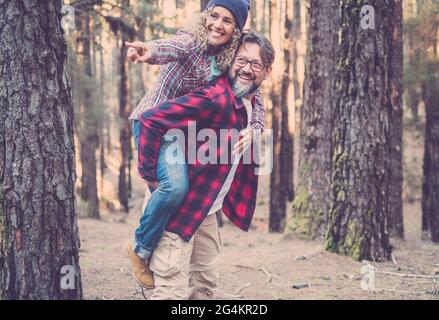 Giocosa felice bella coppia caucasica che ha piggyback mentre cammina su sentiero in boschi. Avventura in natura concetto - giovane adulto uomo e donna enjo Foto Stock