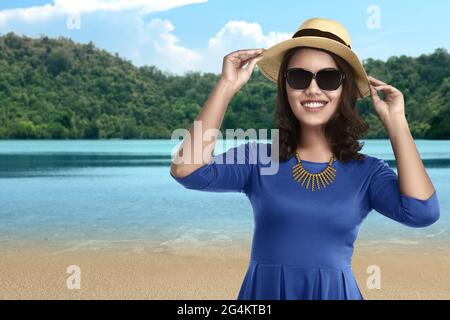 Donna asiatica in piedi con cappello e occhiali da sole sul lago con collina e cielo blu sfondo Foto Stock