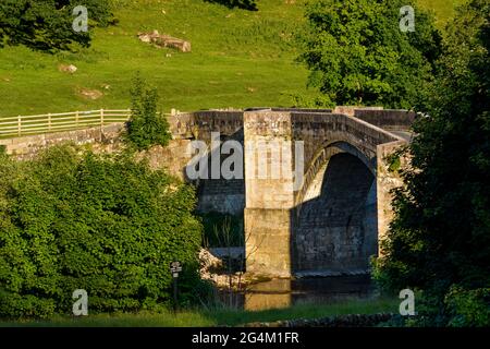 Vista panoramica e soleggiata sul fiume dello storico ponte ad arco in pietra C17 che attraversa il fiume Shallow Wharfe - Barden Bridge, Yorkshire Dales, Inghilterra, Regno Unito. Foto Stock