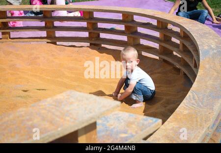 Un bambino di un anno gioca in sandpit con sabbia arancione Foto Stock