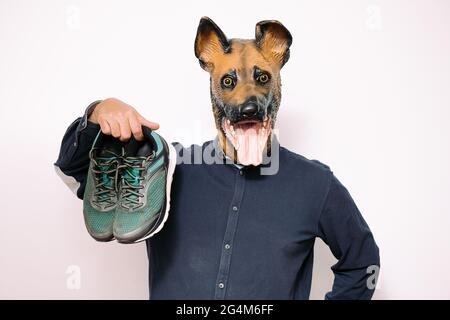 persona con una maschera cane che tiene un paio di scarpe da running su sfondo bianco, concetto di sport e stile di vita attivo con gli animali domestici Foto Stock