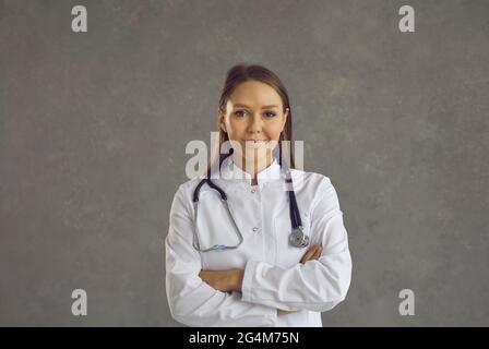 Ritratto di una giovane donna amichevole sorridente operatrice medica su uno sfondo grigio cemento. Foto Stock
