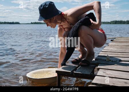 La giovane ragazza lava i vestiti a mano nel bacino. Lavare a mano i vestiti in natura. Lavare i vestiti nel lago. Foto Stock