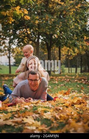 famiglia pretend piramide autunno parco seduta tra gli alberi, sorridente insieme.foglie caduta, stile di vita. Foto Stock