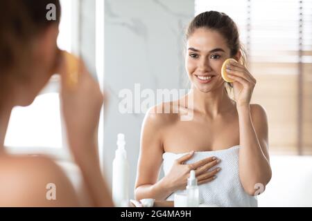 Donna che usa la spugna cosmetica godendo di Skincare facciale routine in bagno Foto Stock