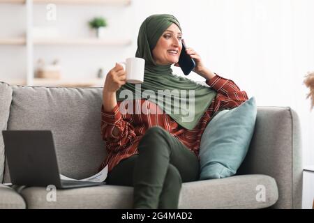 Signora Medio-Orientale matura in Hijab che parla su Cellphone a casa Foto Stock